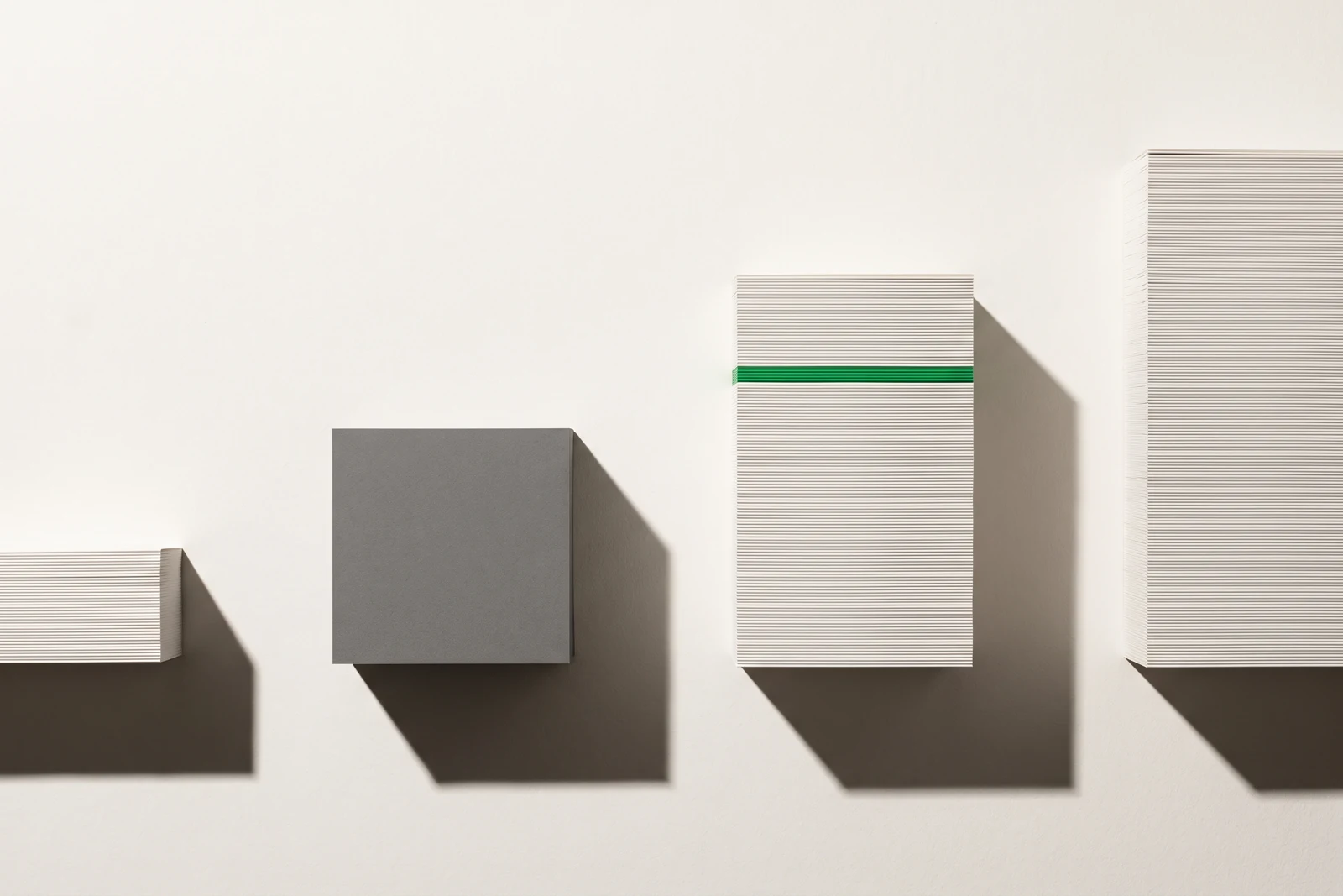 Quatre piles de papier blanc d’épaisseurs inégales vues de face, la deuxième remplacée par un bloc de carton gris, une fine tranche verte insérée dans la troisième.
