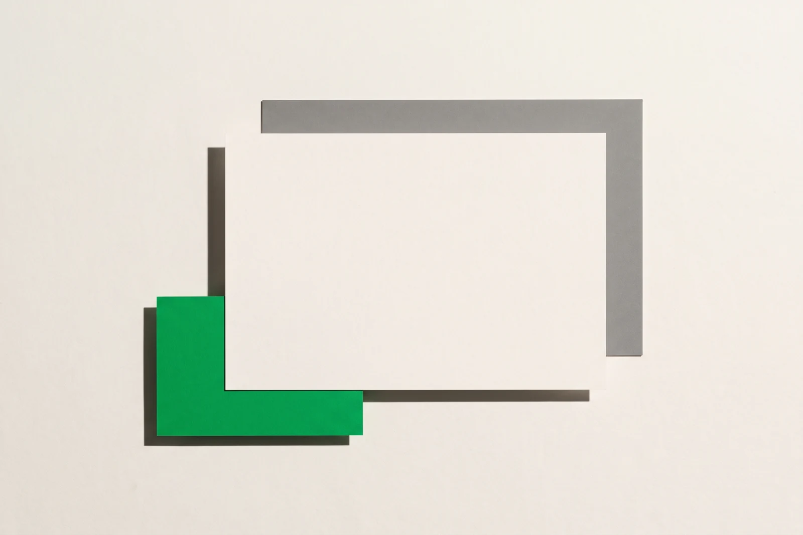 Vue à plat : une petite carte verte glissée à moitié sous une grande feuille de papier blanc, un aplat de carton gris dépassant en haut à droite.