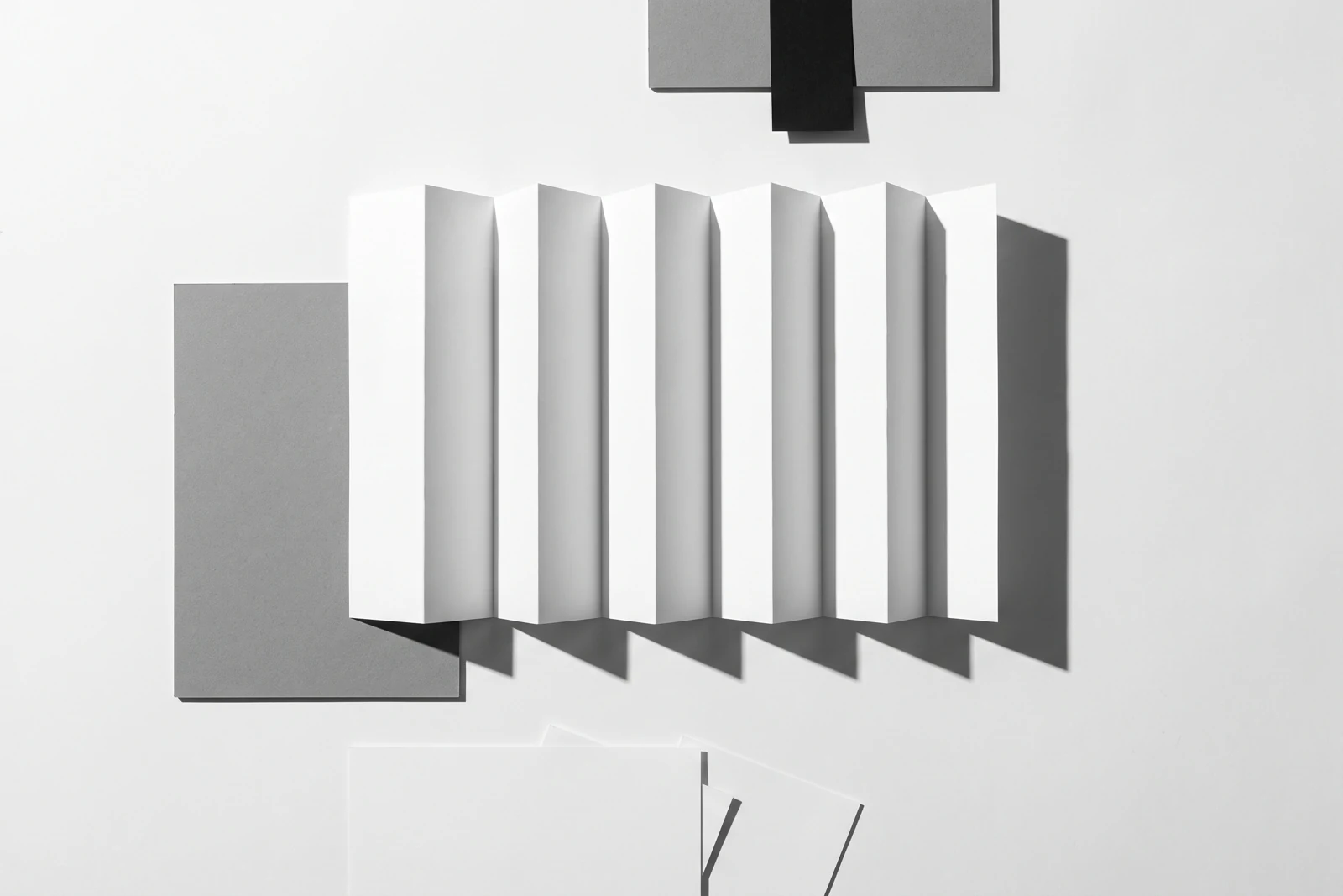 Une feuille de papier fin pliée en accordéon à arêtes vives, ombres dures projetées vers le bas à droite.