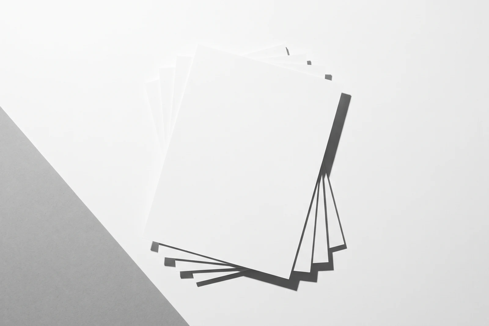 Des feuilles de papier fin empilées à plat et visiblement désalignées, ombres dures projetées vers le bas à droite.