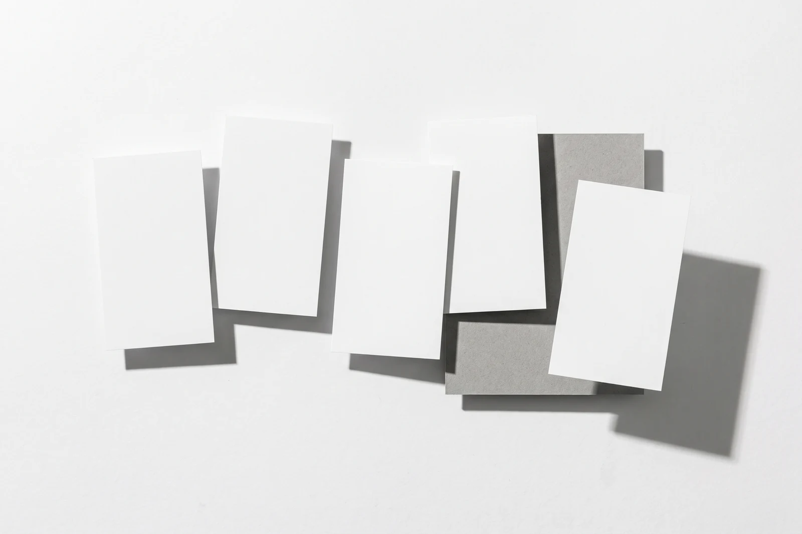 Une rangée de cartes de papier qui dérive progressivement hors de l’axe, ombres dures projetées vers le bas à droite.