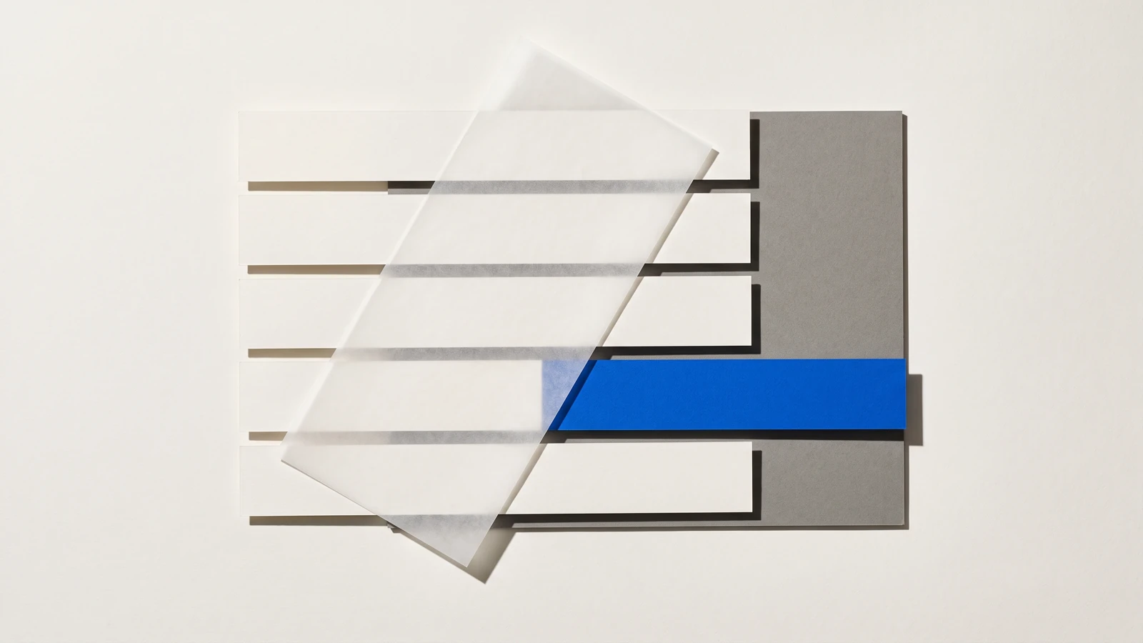 Un calque cristal posé de biais sur des feuilles de papier vierge, ombres dures projetées vers le bas à droite.