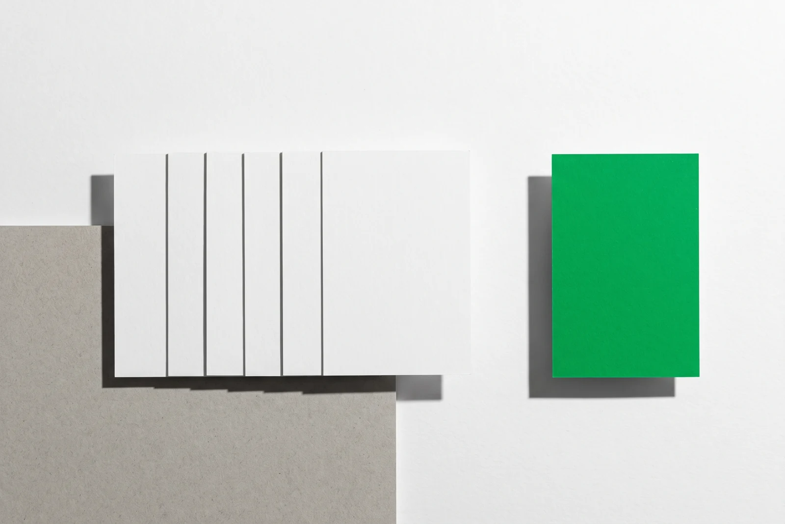 Un groupe serré de cartes de papier vierge et une carte isolée à l’écart, ombres dures projetées vers le bas à droite.