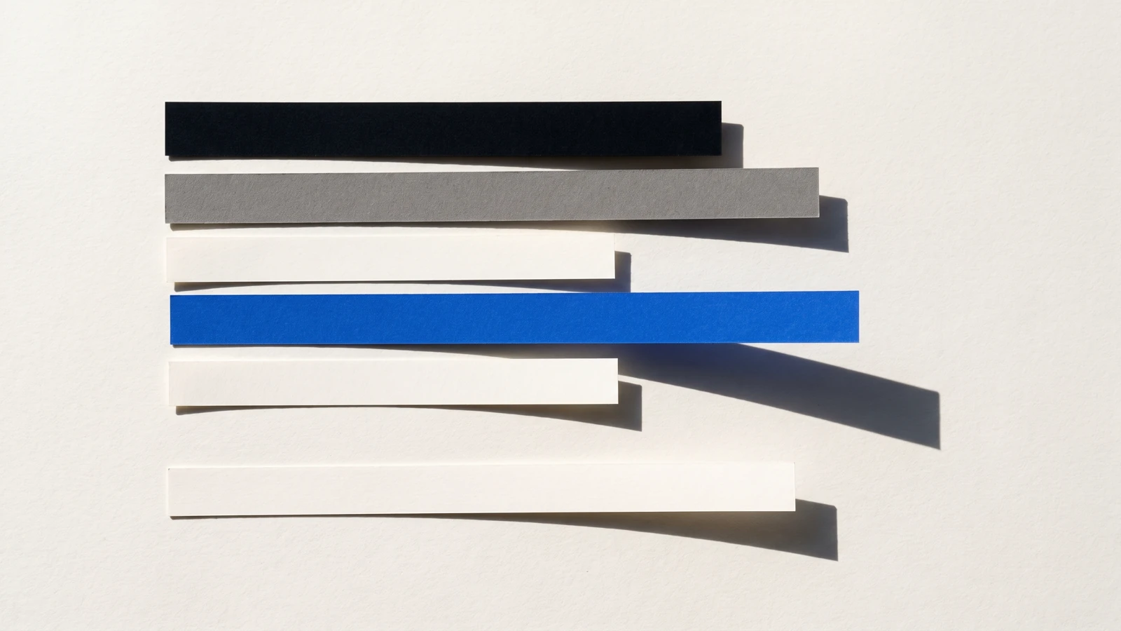 Une carte glissée hors d’une pile de papier vierge et qui dépasse nettement, ombres dures projetées vers le bas à droite.