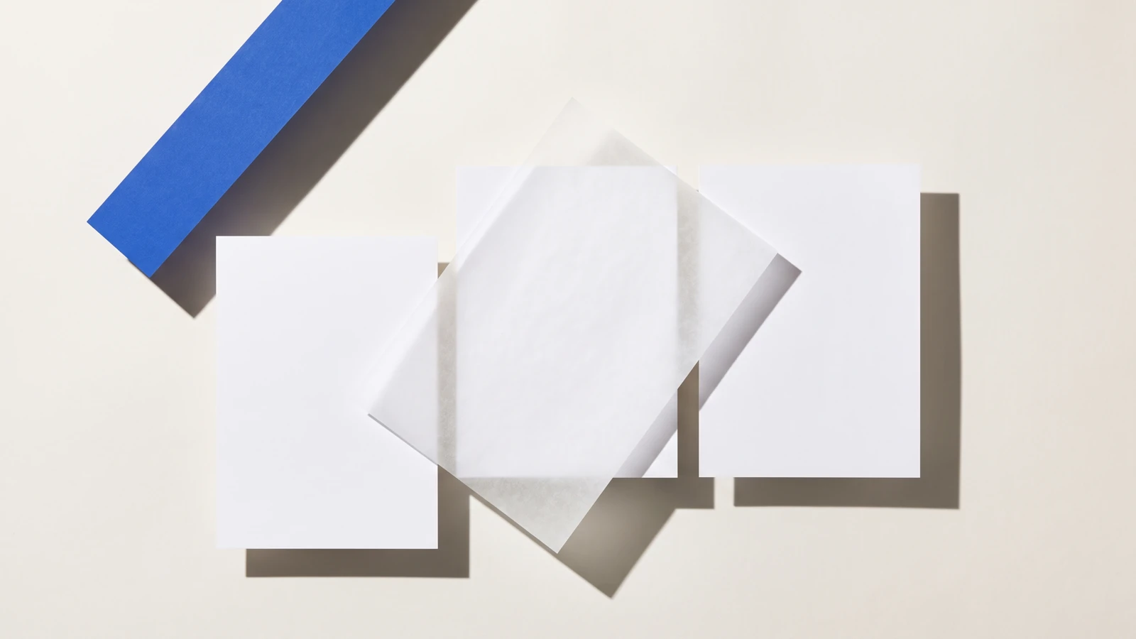 Une carte glissée hors d’une pile de papier vierge et qui dépasse nettement, ombres dures projetées vers le bas à droite.