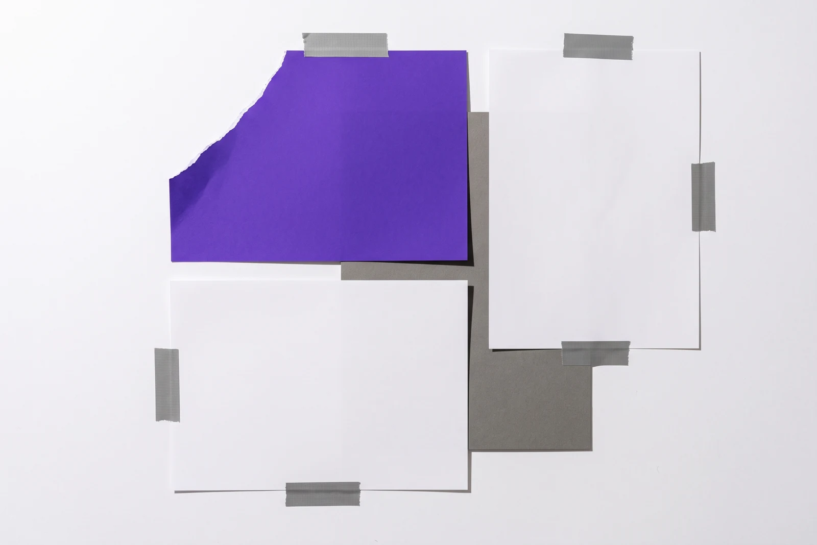 Des feuilles de papier scotchées à plat, le coin de la feuille du dessus arraché, ombres dures projetées vers le bas à droite.