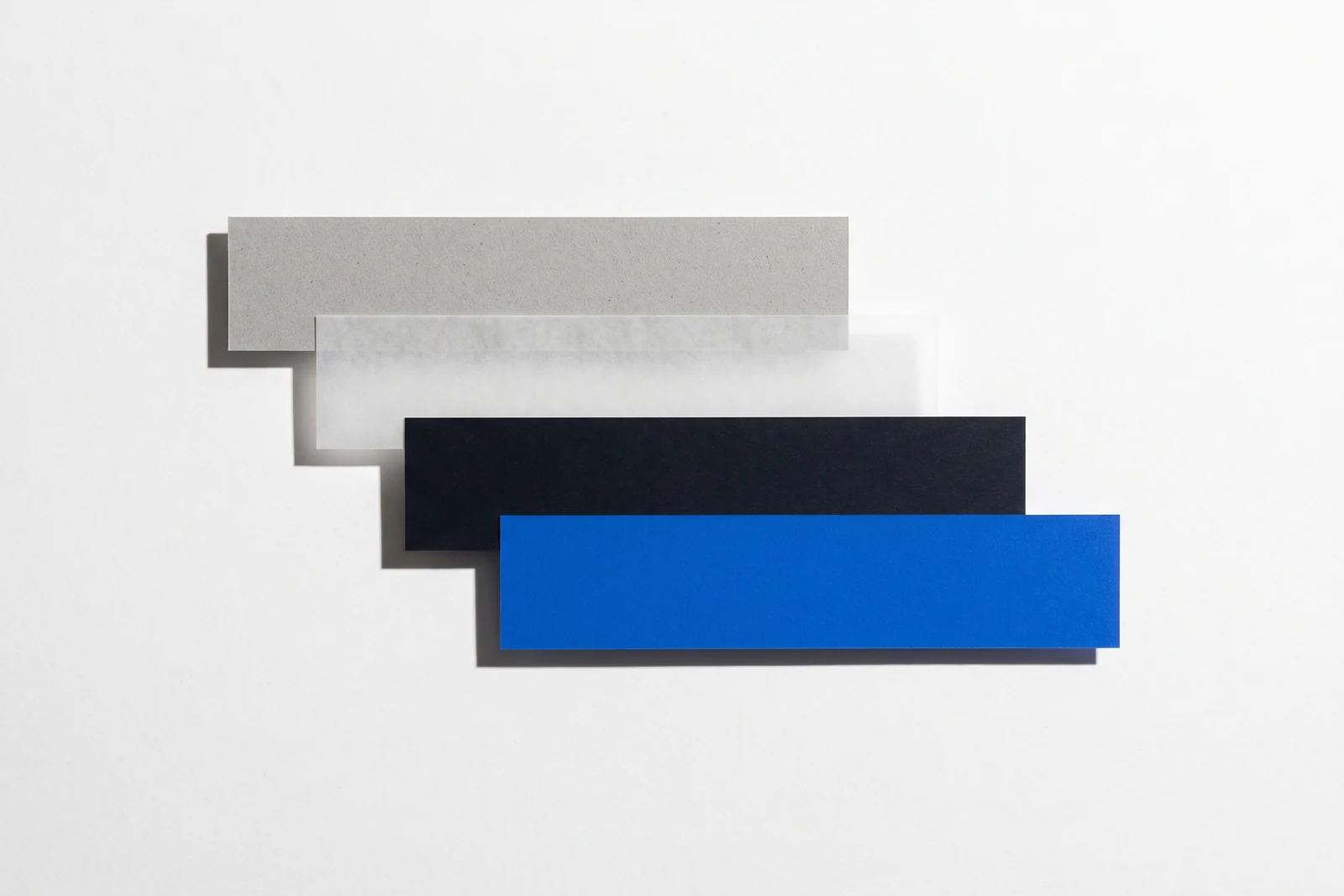Des pièces de papier vierge disposées en escalier descendant, ombres dures projetées vers le bas à droite.