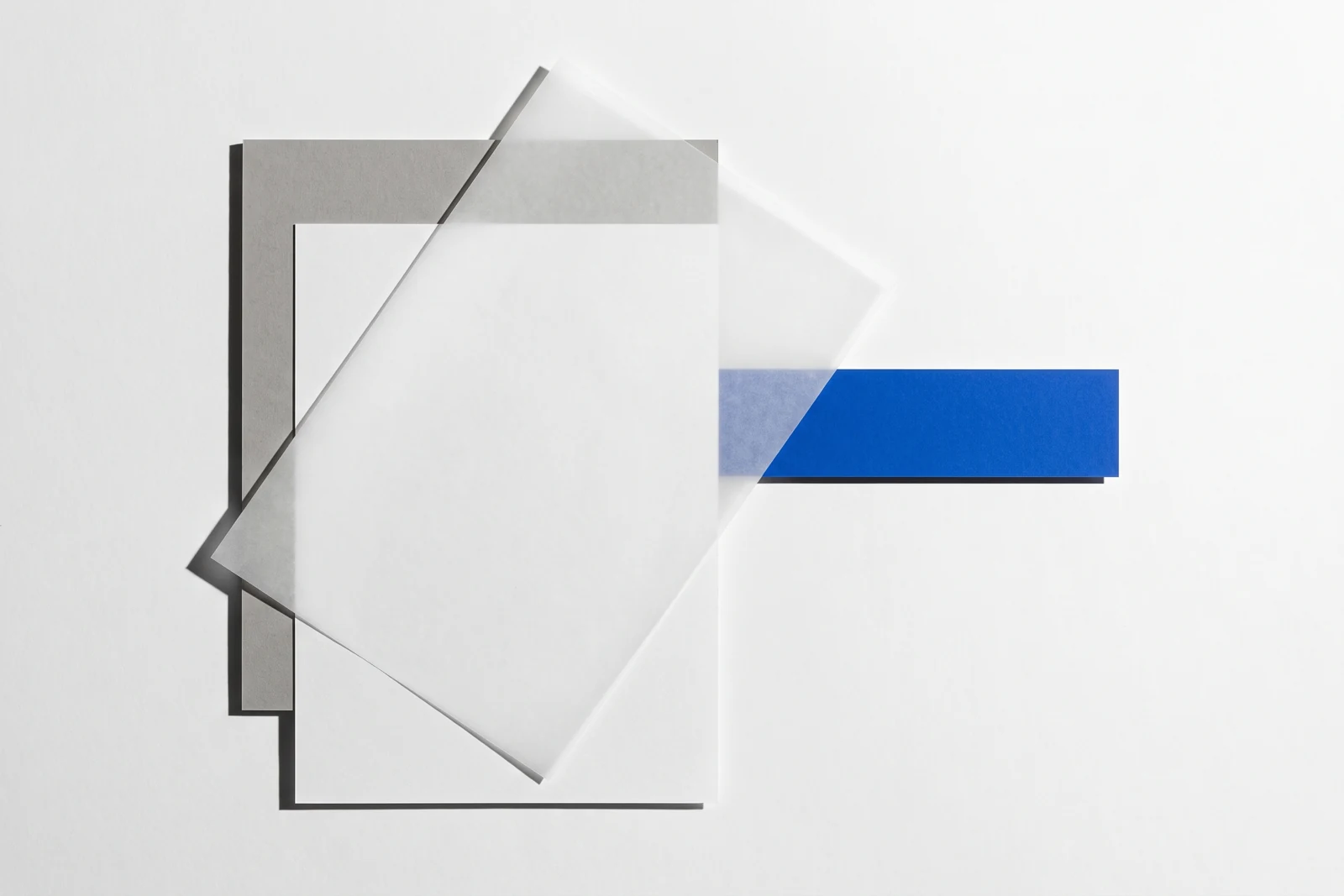 Un calque cristal posé de biais sur des feuilles de papier vierge, ombres dures projetées vers le bas à droite.