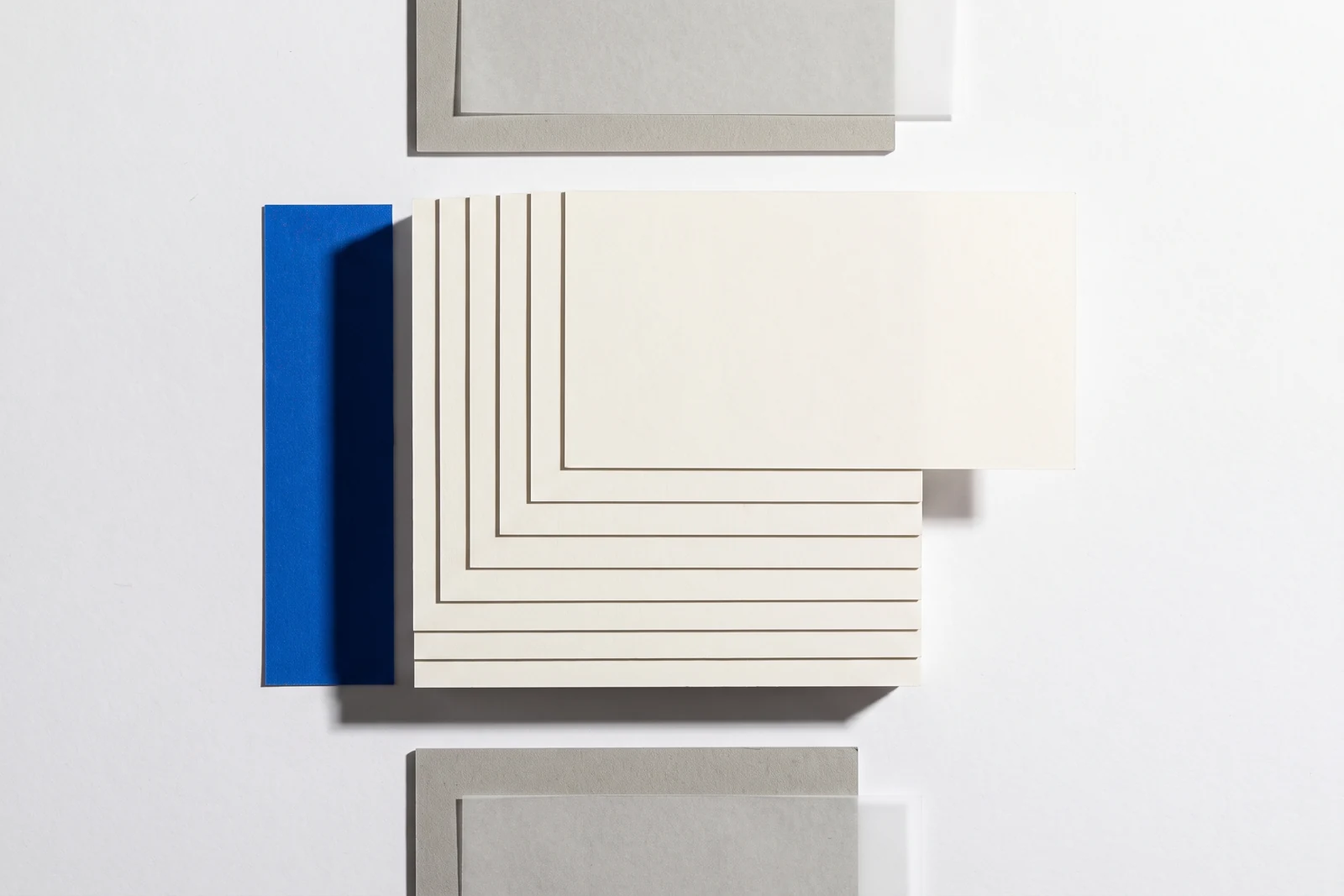 Une carte glissée hors d’une pile de papier vierge et qui dépasse nettement, ombres dures projetées vers le bas à droite.