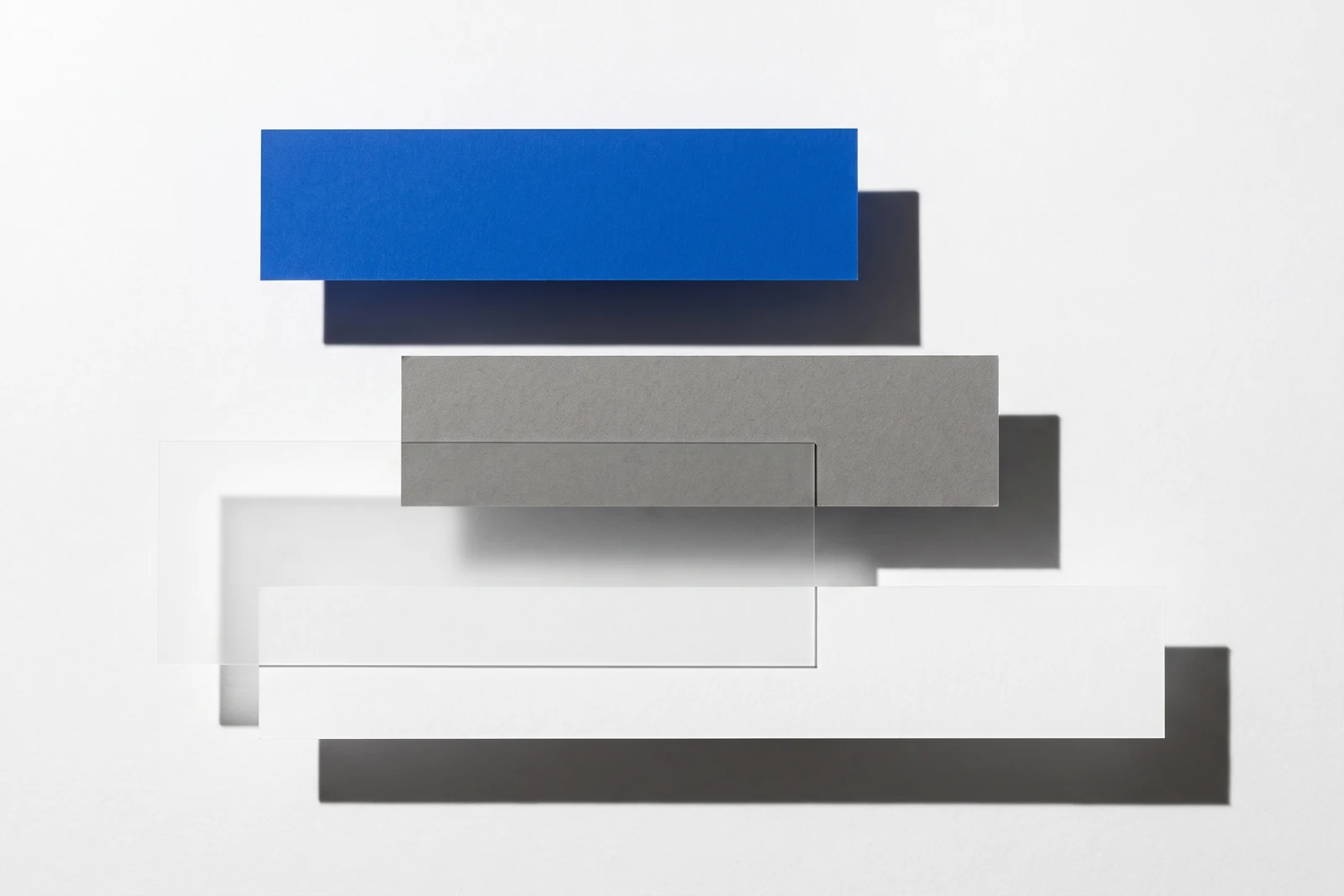 Des pièces de papier vierge disposées en escalier descendant, ombres dures projetées vers le bas à droite.